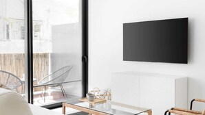 Ein modernes Wohnzimmer mit einer Couch, zwei Korbstühlen, einem Couchtisch und einem flachbildfernseher an der Wand.