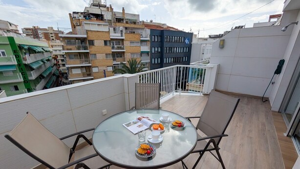 A round glass table with four chairs on a balcony, overlooking a cityscape with multi-story buildings. - ROQUET rooftop heart of Benidorm (Benidorm)