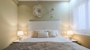 A bedroom with a large bed, two bedside tables with lamps, a wall-mounted flower decoration, and a window with sheer curtains. - ROQUET rooftop heart of Benidorm (Benidorm)