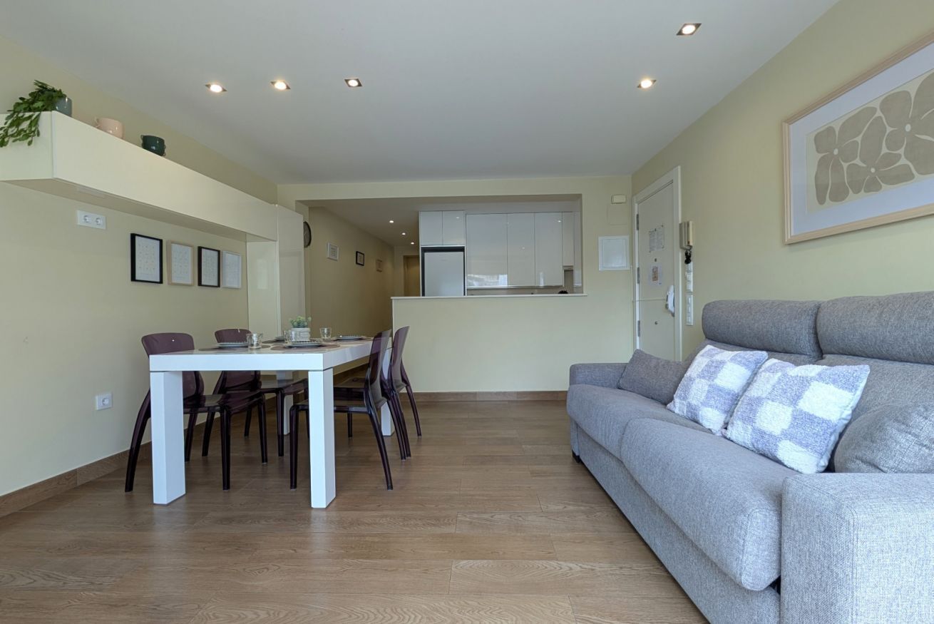 A modern apartment with a dining area, a gray sofa, and a kitchen in the background.
