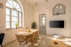 Ein Essbereich mit einem runden Tisch, Korbstühlen, einem an der Wand montierten Fernseher und einem großen Fenster mit Ausblick.