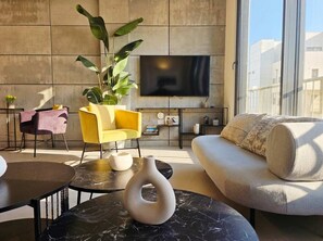 A modern living room with a sofa, yellow armchair, and a large TV on the wall. - Stunning #TLV Rooftop 3BR/2BA | By SweetyGuest (Tel Aviv-Yafo)
