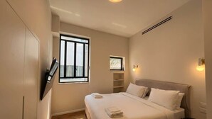 Ein modernes Schlafzimmer mit einem großen Bett, einem an der Wand montierten Fernseher und einem Fenster, das für natürliches Licht sorgt.