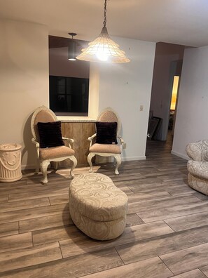 Un salon avec deux fauteuils richement décorés, un pouf rond et un luminaire suspendu.