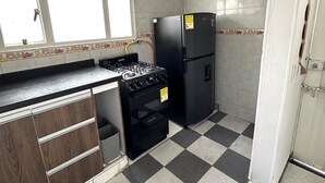 Una cocina compacta con estufa a gas, refrigerador negro y ventana con azulejos decorativos.