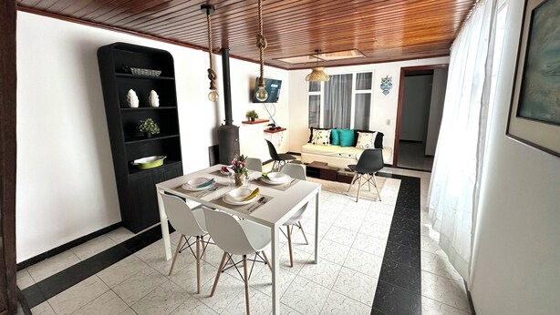 Un espacio habitable moderno con comedor, una estantería negra y una zona de estar acogedora con sofá y cojines.