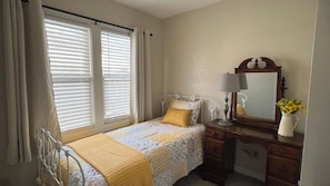 A bedroom with a bed, bedside table, lamp, mirror, and a window with blinds. - The Orange Door Boarding House (Guthrie)
