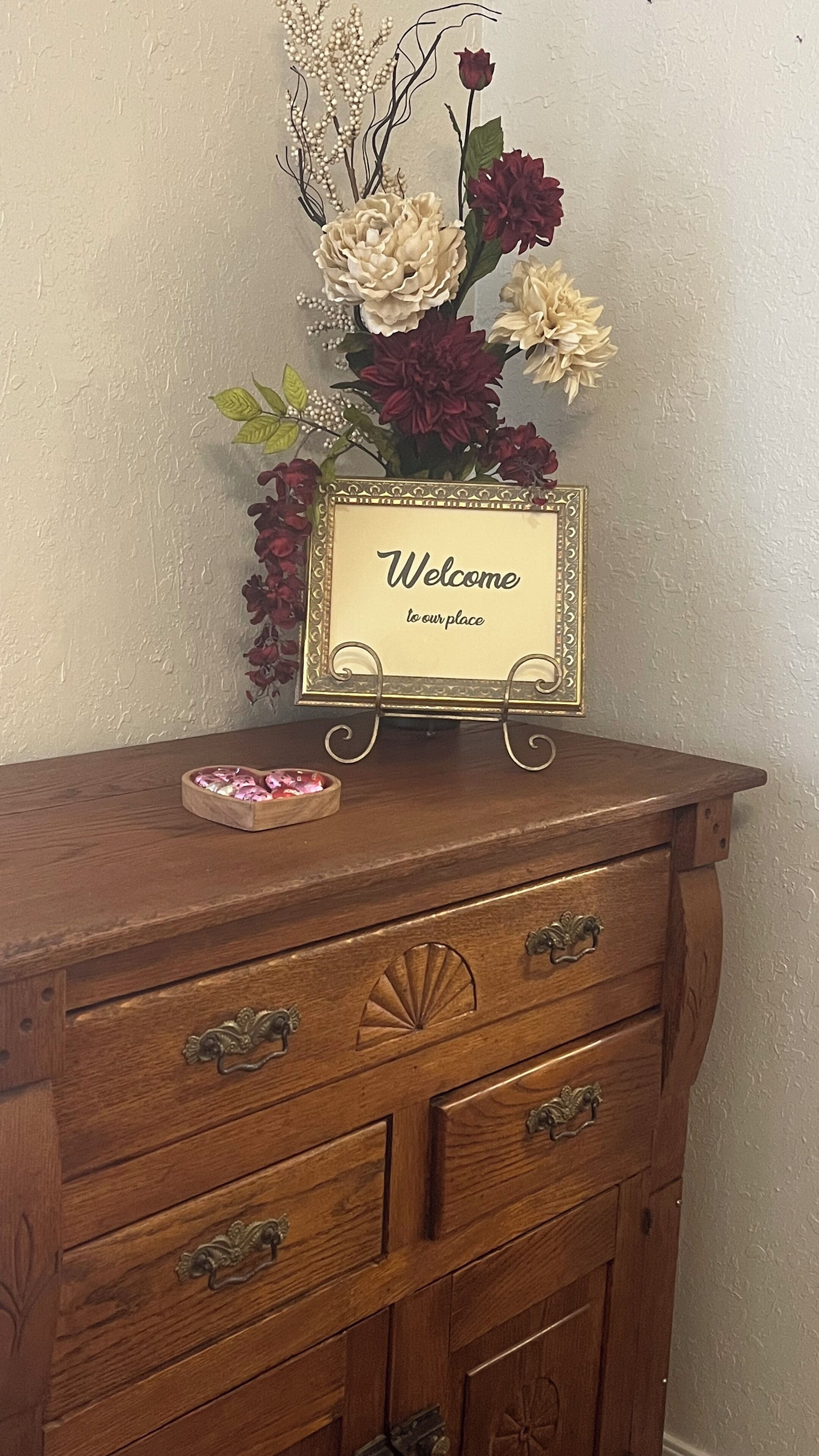 A wooden dresser with a decorative sign that reads "Welcome to our place."