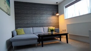 Una sala de estar moderna con un sofá gris, una mesa de centro negra y una pared oscura con textura.