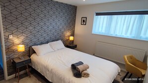 Habitación de hotel con cama, dos mesitas de noche con lámparas, una ventana con persianas, un radiador y una silla.