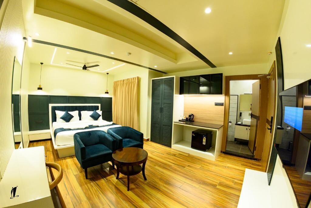 Quarto de hotel moderno com uma cama, dois sofás, uma mesa pequena, uma televisão e uma cozinha compacta.