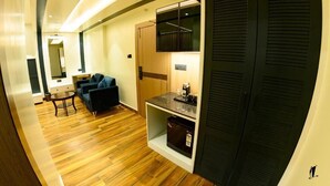 Une chambre d’hôtel avec un plancher en bois, un canapé, une table basse, un minibar et une armoire aux portes à persiennes.