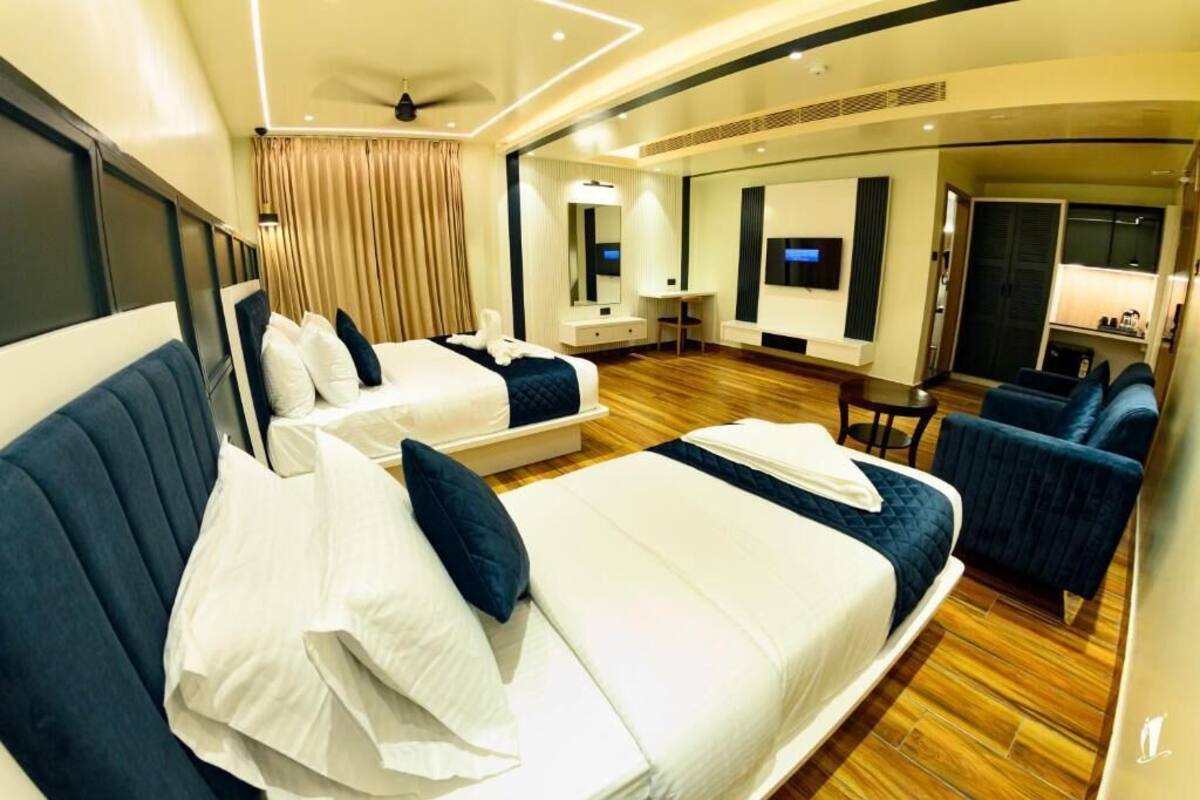 Quarto de hotel com duas camas, uma mesa de trabalho, televisão e área de estar.