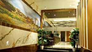Un hall d’hôtel avec un mur de marbre, une fresque murale et des plantes en pot.