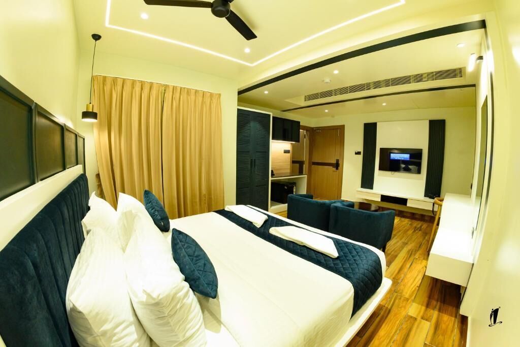 Camera d'albergo moderna con un ampio letto, una ventola a soffitto, una TV e un angolo salotto con tavolo e sedie.