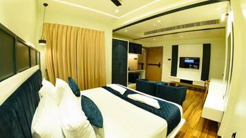Camera d'albergo moderna con un ampio letto, una ventola a soffitto, una TV e un angolo salotto con tavolo e sedie.