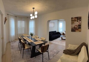 Een moderne woonkamer met een eethoek, met een zwarte eettafel, beige stoelen, een zwarte bank en een beige fauteuil.
