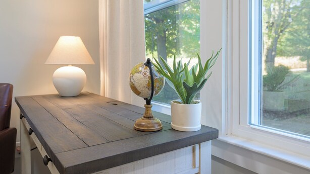 Une table en bois, sur laquelle se trouvent un globe terrestre et une plante en pot, près d’une fenêtre.