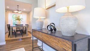 Un salon moderne avec une console en bois, deux lampes et un coin repas comprenant une table et des chaises.