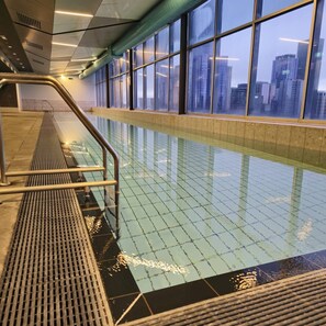 An indoor swimming pool with a clear view of the cityscape through large windows. - Deluxe 2BR apt Excellent Location Cityviews & Pool (Melbourne)