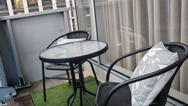 A balcony with a glass table and two chairs, artificial grass flooring, and a view of a cityscape through large windows. - Deluxe 2BR apt Excellent Location Cityviews & Pool (Melbourne)