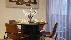 A dining area with a round table, four chairs, a vase with flowers, and a large abstract painting on the wall. - Deluxe 2BR apt Excellent Location Cityviews & Pool (Melbourne)