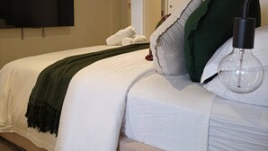 A neatly made bed with a white comforter and a dark green throw blanket. A clear glass light bulb hangs above the bed, and there are pillows in shades of green and white. - Deluxe 2BR apt Excellent Location Cityviews & Pool (Melbourne)