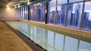 An indoor swimming pool with a view of city buildings through large windows. - Deluxe 2BR apt Excellent Location Cityviews & Pool (Melbourne)