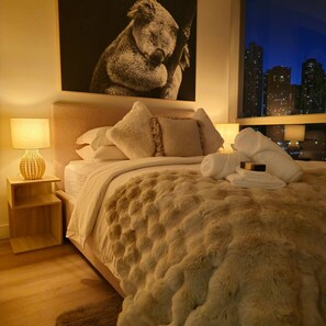 A hotel room with a large bed, fluffy white bedding, a cityscape view, and a decorative lamp. - Deluxe 2BR apt Excellent Location Cityviews & Pool (Melbourne)