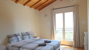Een slaapkamer met een houten plafond, een bed met een geruite sprei, een donker vloerkleed en een raam met gordijnen.