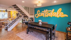 A spacious living area with a staircase, a dining table with benches, and a wall with the word "Scottsdale" painted on it. - Walk to Old Town! Pool, Arcade & Mini Golf - 6 beds (Scottsdale)