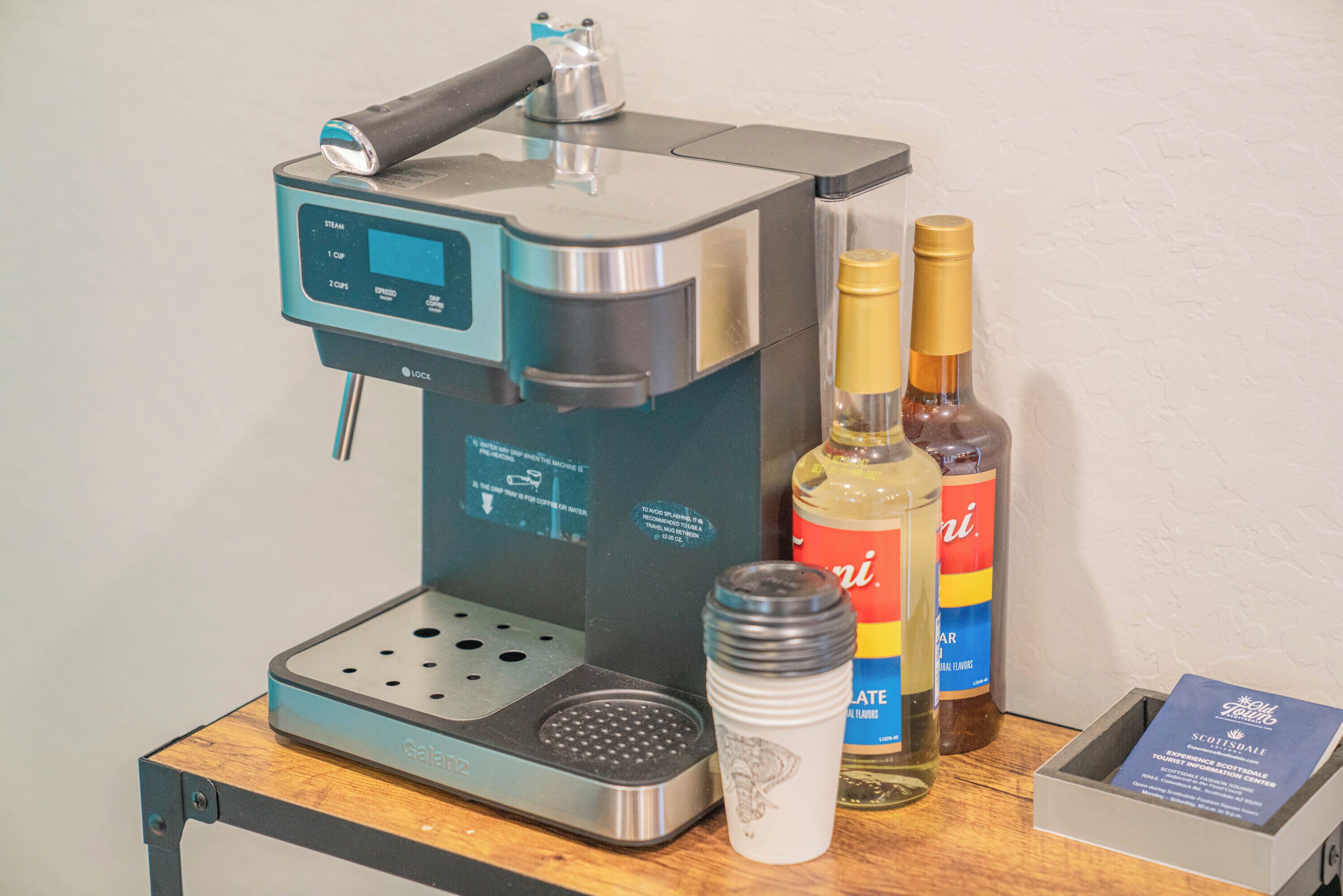 A coffee machine, a tumbler, and two bottles of liquor on a wooden table.
