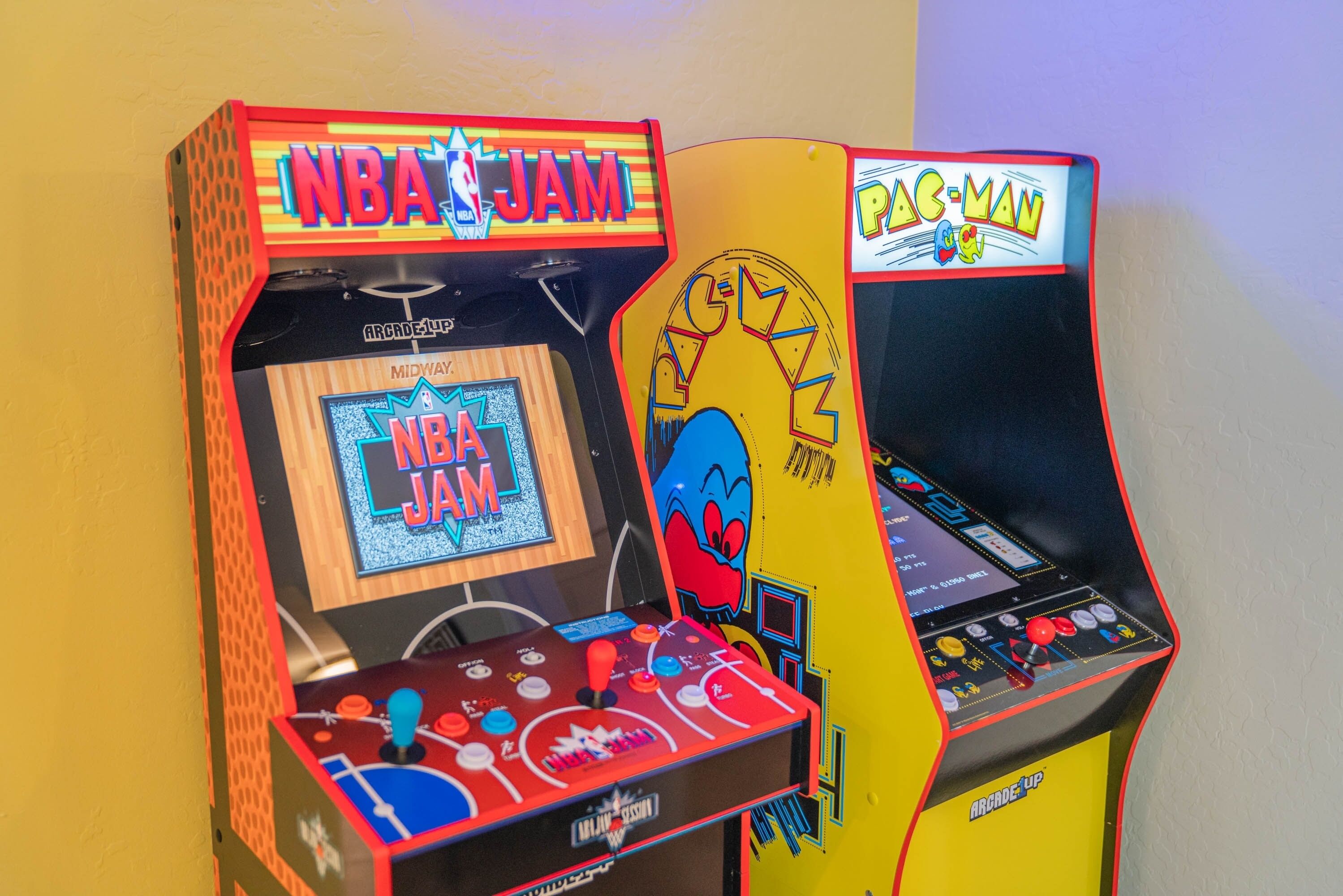 Two arcade machines, one labeled NBA JAM and the other Pac-Man, with colorful graphics and joystick controls.