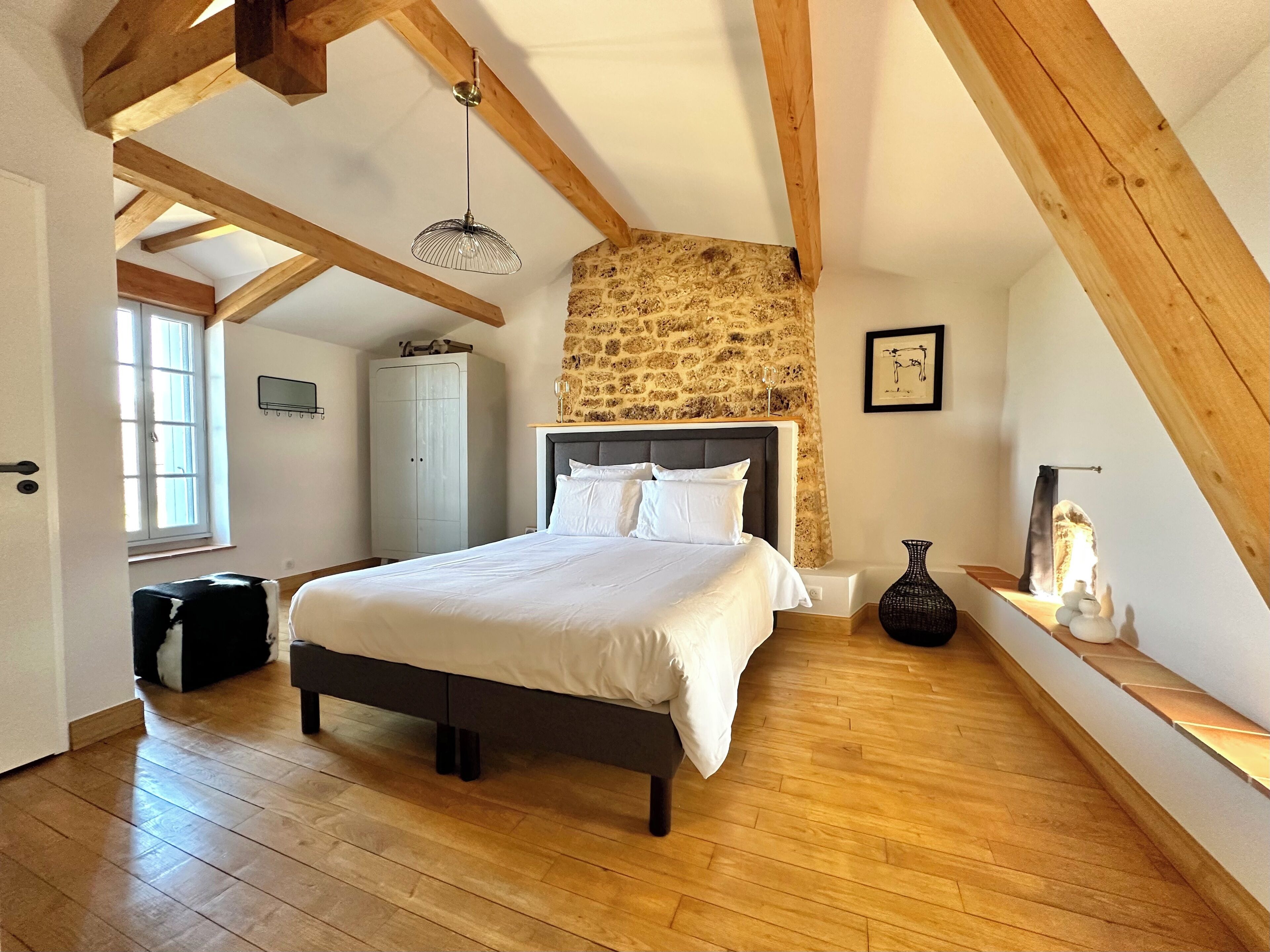 Een slaapkamer met een groot bed, houten balken, een stenen muur en een raam.