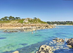 A coastal landscape with clear turquoise waters, rocky outcrops, and a distant hill with sparse vegetation. - Degemer mat! Typical Breton house renovated (Trébeurden)
