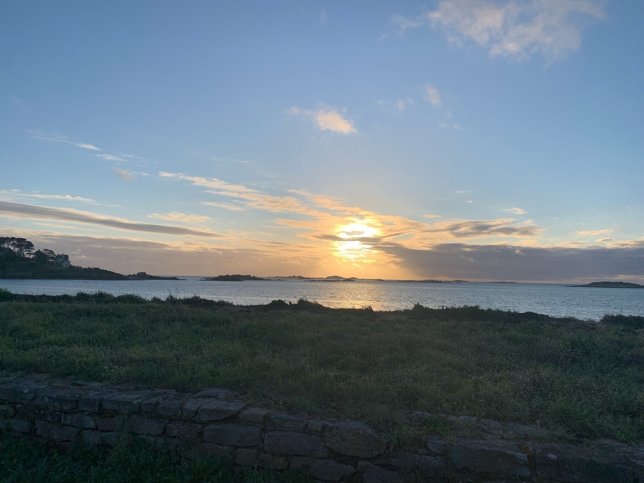 A sunset over a calm body of water with a stone wall in the foreground.