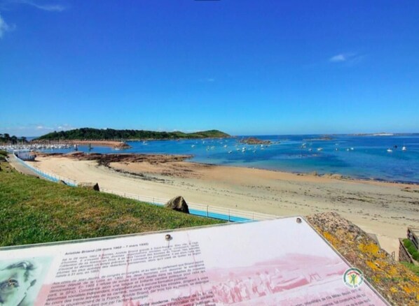 Una vista sulla costa con spiaggia, cielo azzurro limpido e un cartello segnaletico.