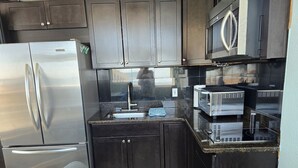 Una cocina compacta con armarios oscuros, un refrigerador de acero inoxidable, un microondas y un tostador.