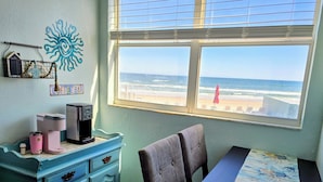 Habitación con vista a la playa, cafetera, mesa con mantel y cómoda azul.
