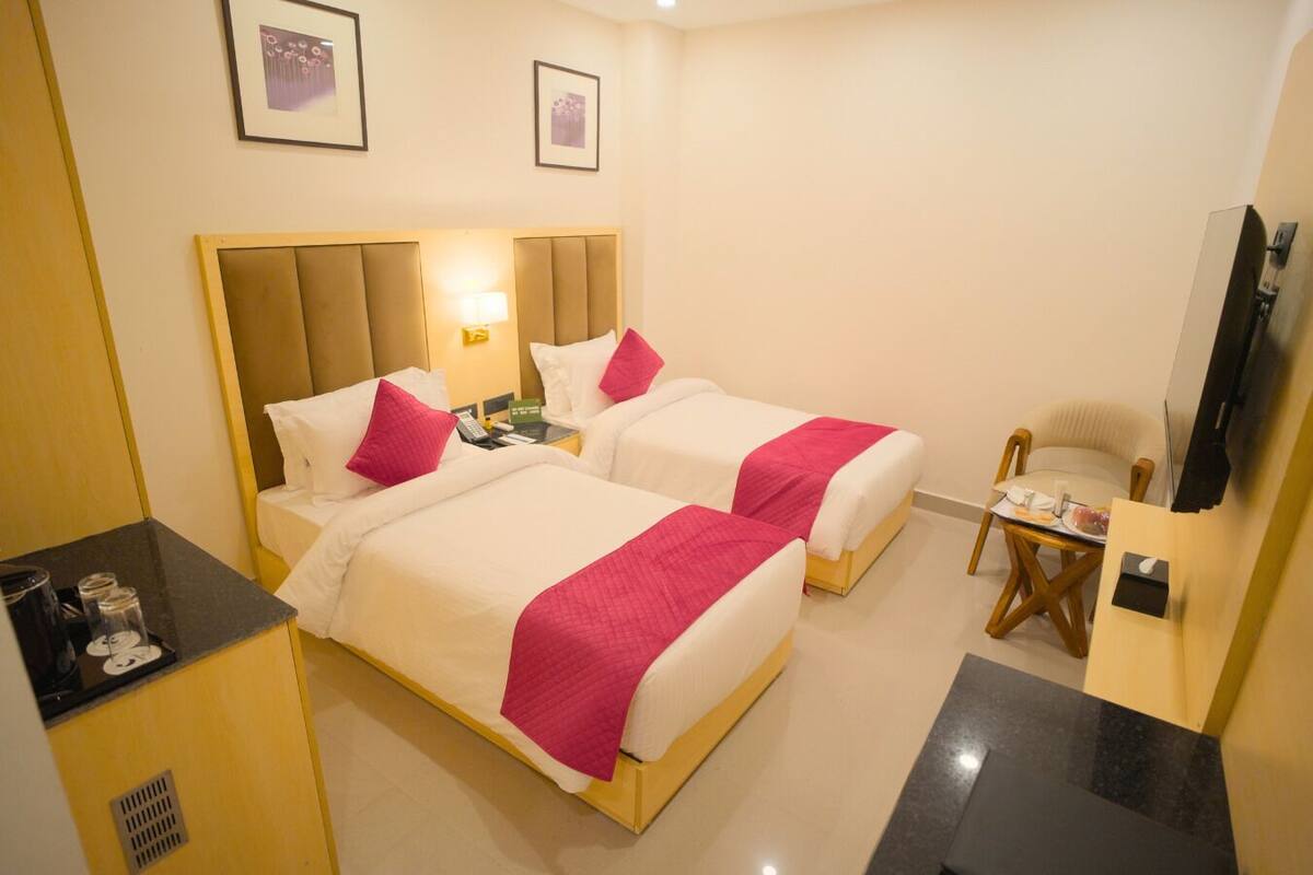 Una habitación de hotel con dos camas, un escritorio, una silla, un televisor y un minibar.