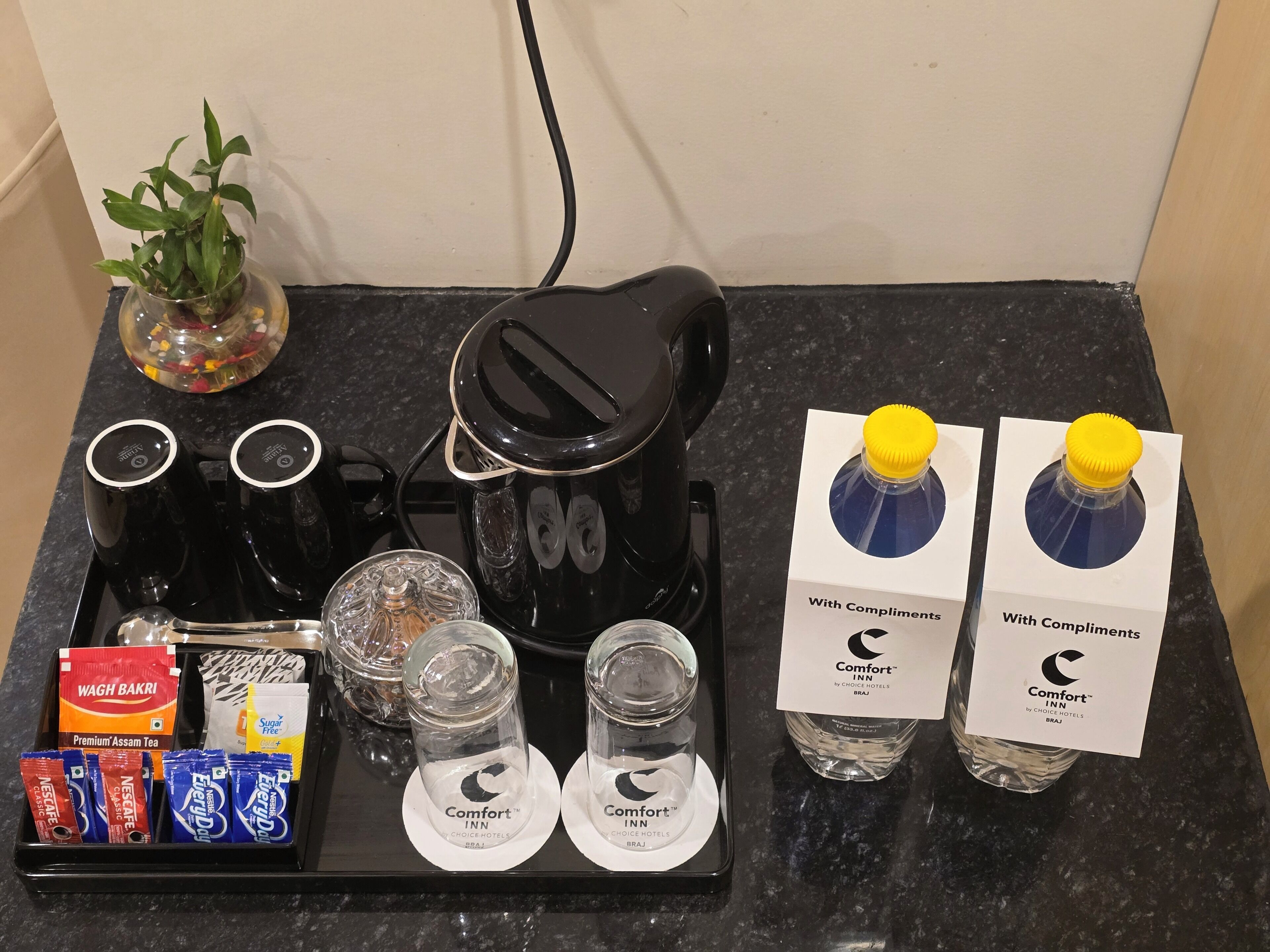 A coffee maker, tea packets, sugar packets, and two bottles of water with complimentary labels.