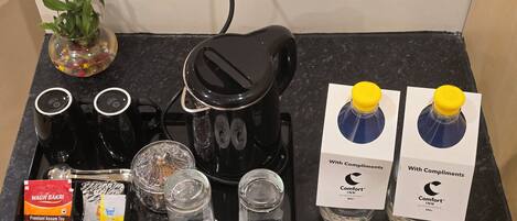 A coffee maker, tea packets, sugar packets, and two bottles of water with complimentary labels.