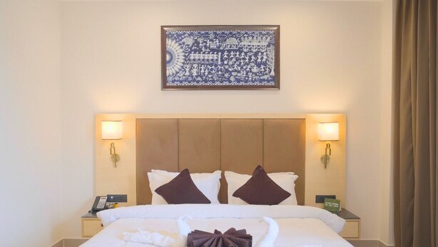Ein Hotelzimmer mit einem großen Bett, zwei Nachttischlampen, einem Deckenventilator und einem gerahmten Kunstwerk über dem Bett.