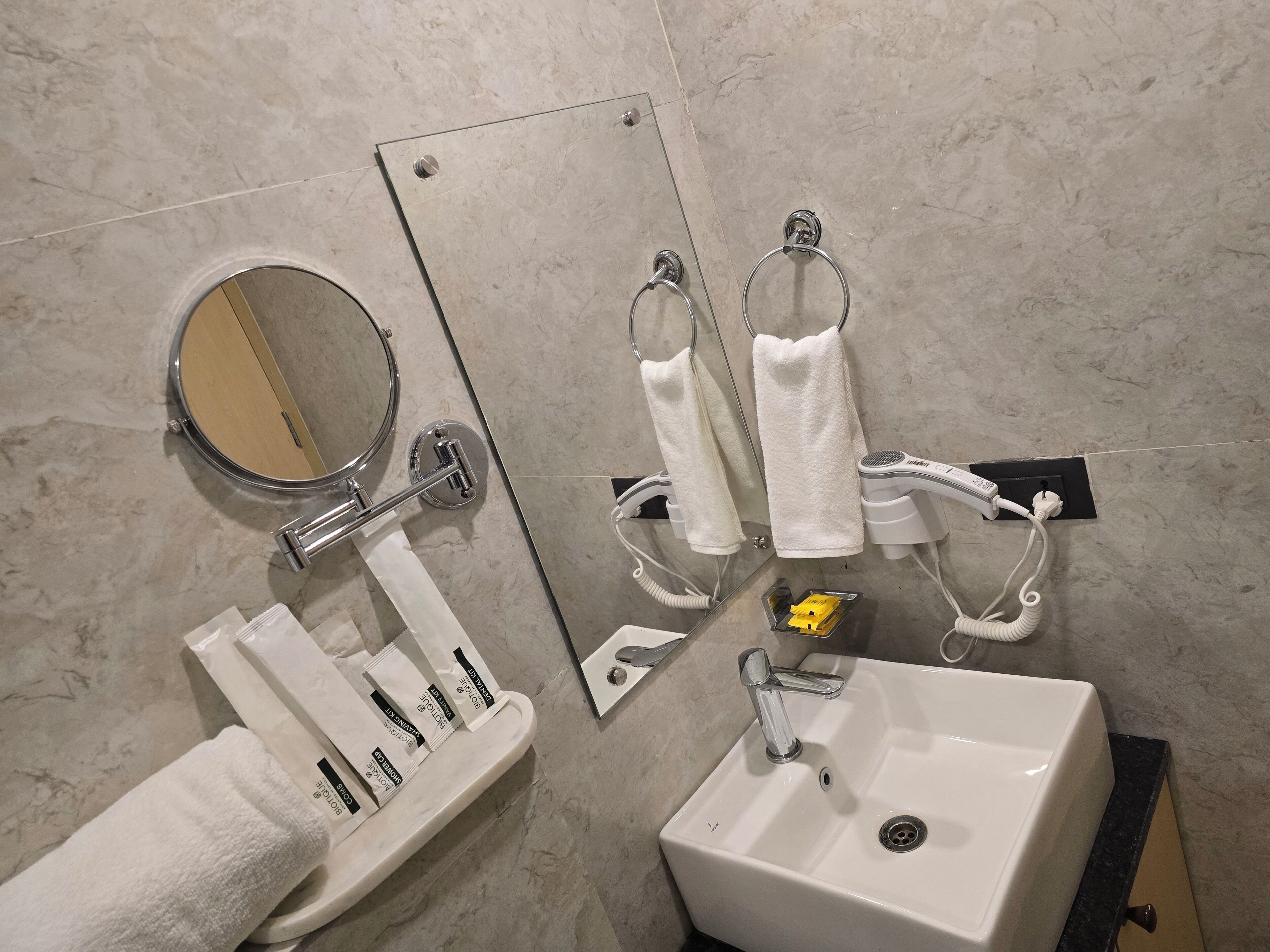 Un baño con lavabo, espejo, toallero y un secador de pelo enchufado.