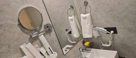 Un baño con lavabo, espejo, toallero y un secador de pelo enchufado.