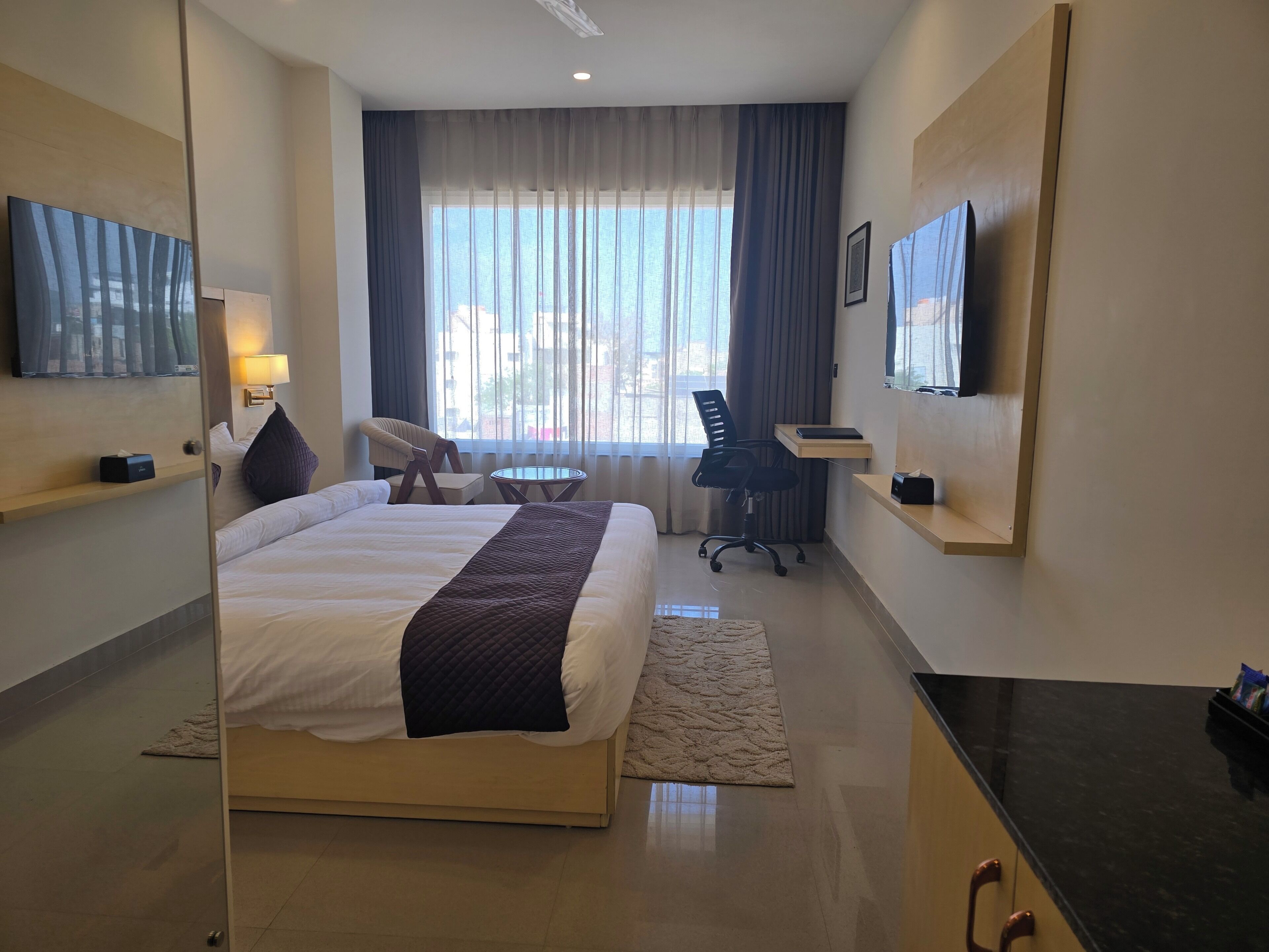 Ein Hotelzimmer mit einem Bett, einem Schreibtisch, einem Sessel, einem Fernseher und einem Fenster mit Vorhängen.
