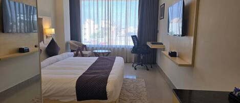 A hotel room with a bed, a desk, a chair, a TV, and a window with curtains.