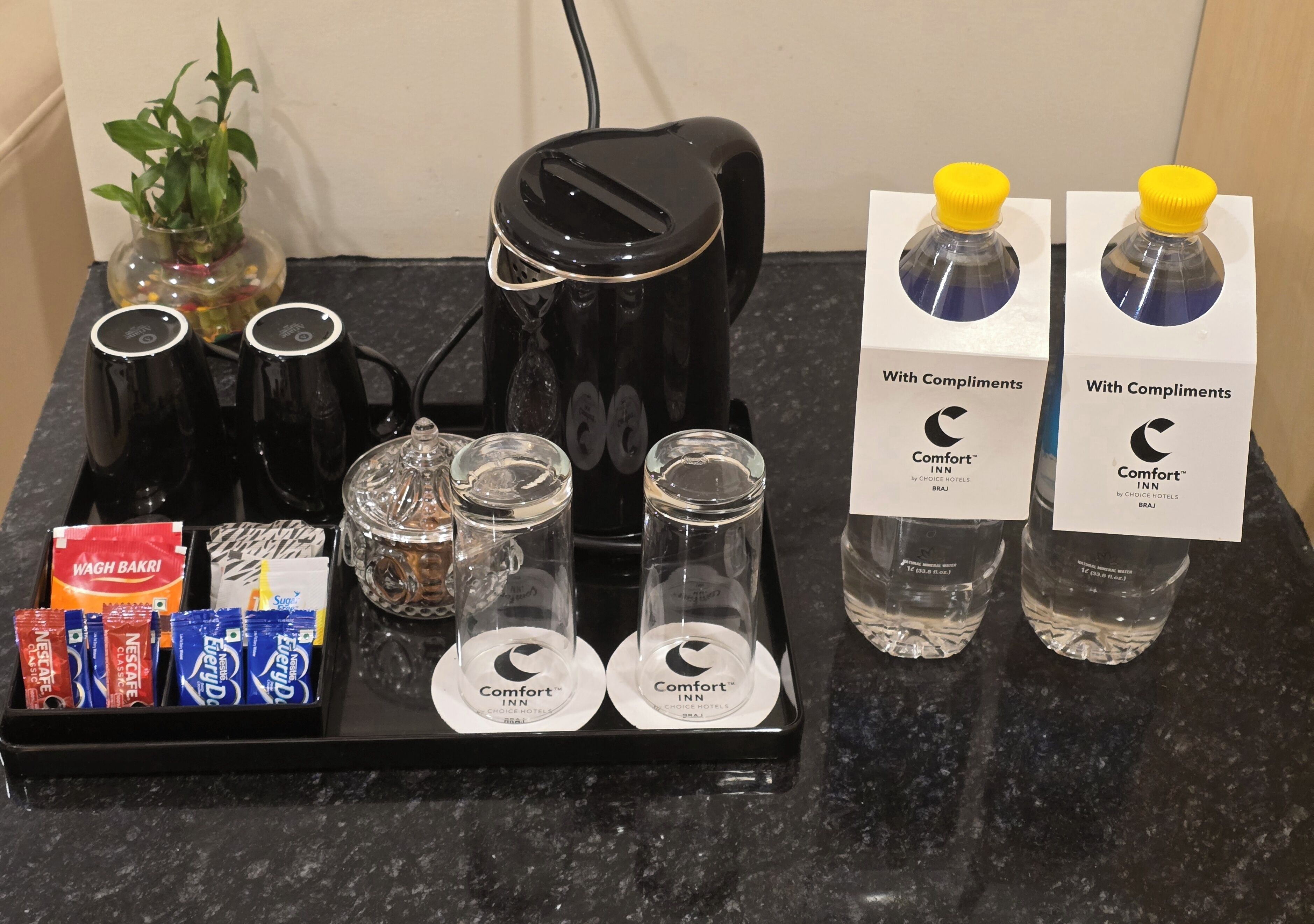 A tray with coffee maker, glasses, water bottles, and snack packets.