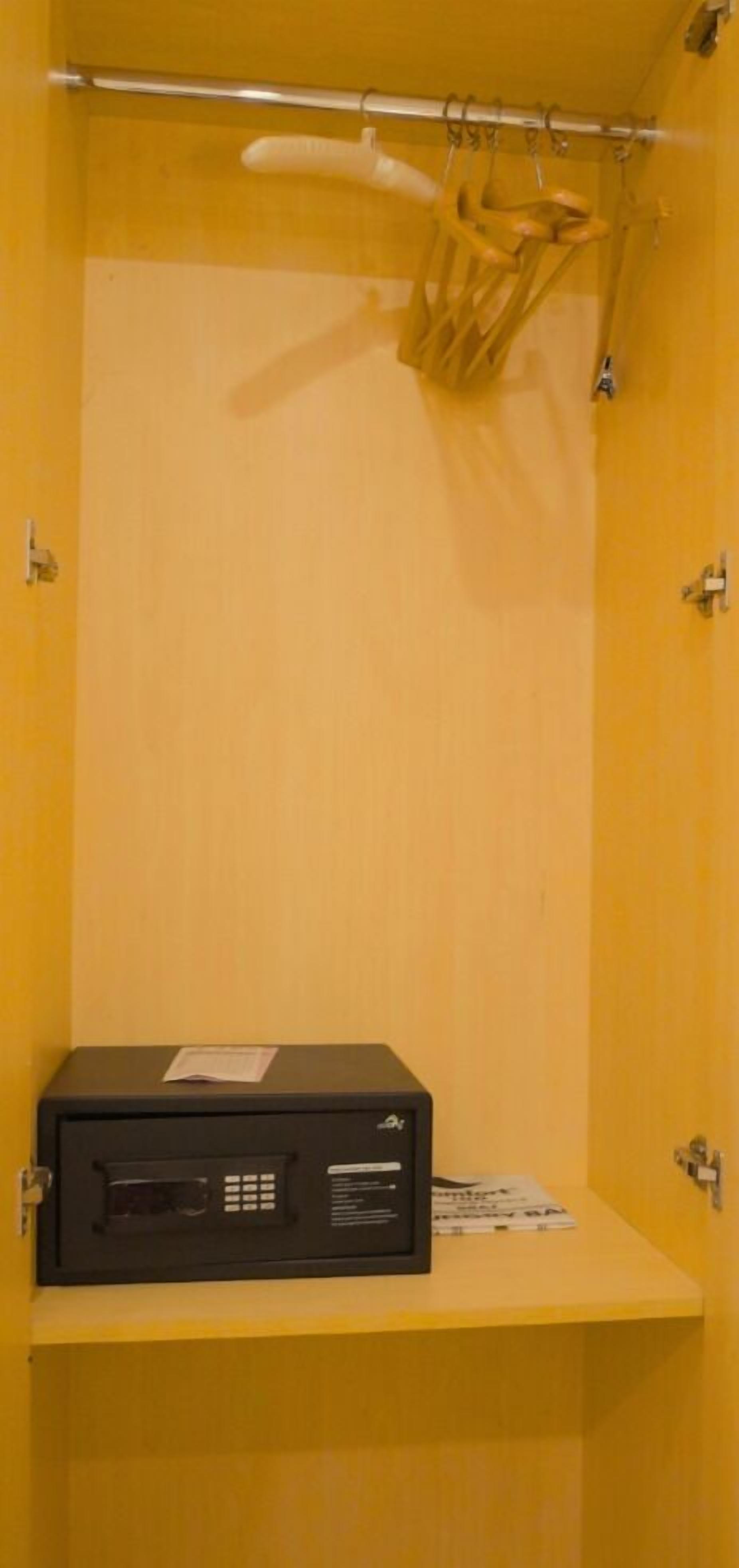 Una habitación con una pared amarilla, un dispositivo electrónico negro sobre una estantería y un perchero con objetos colgados.