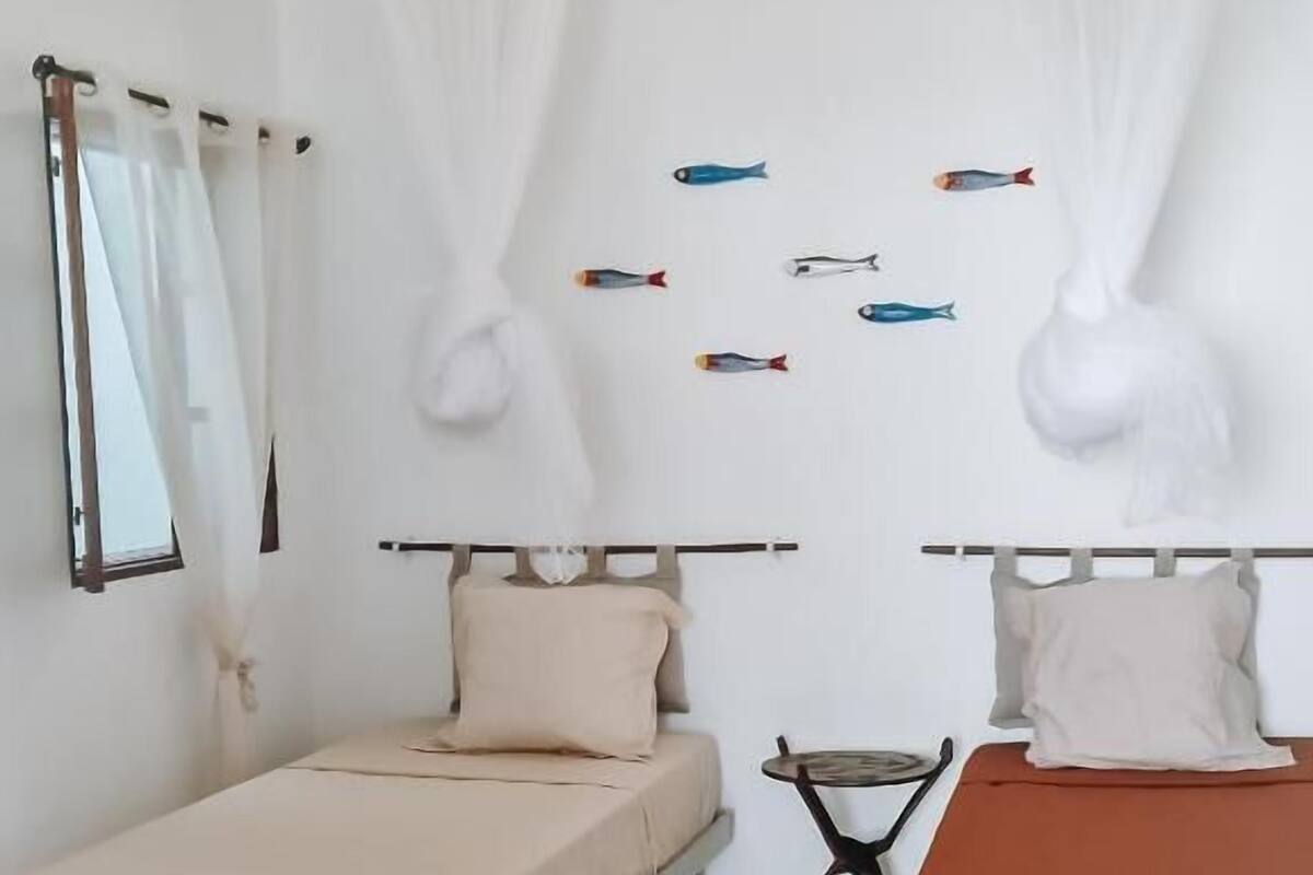 A bedroom with two beds, a ceiling fan, a window with curtains, and wall art.